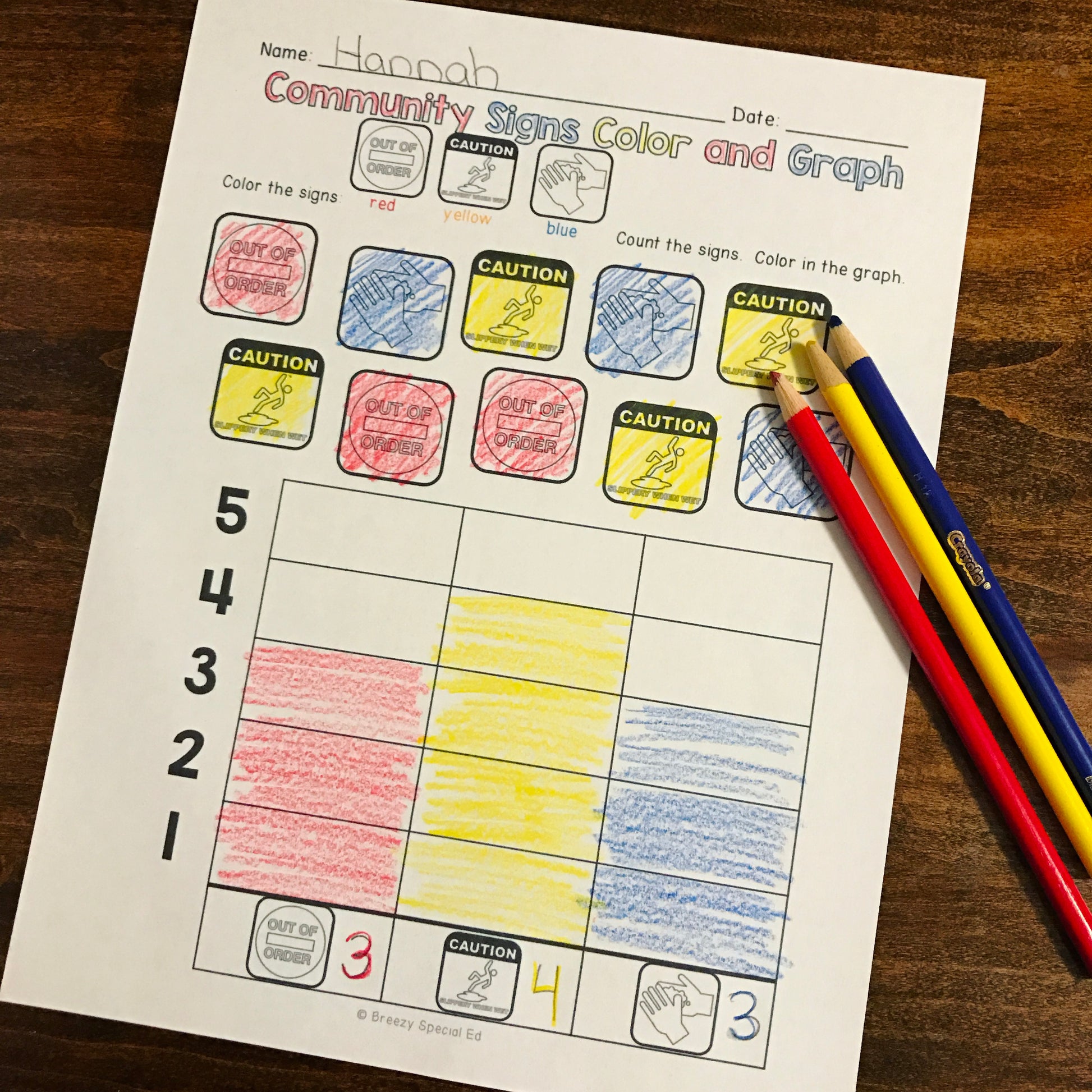Special Education worksheet titled 'Community Signs Color and Graph' with colored pencils on a wooden surface.
