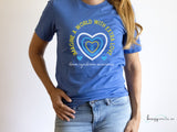 Model wearing a blue Down Syndrome Awareness shirt with yellow, blue and white outlined hearts and arrows in the middle. Text around the heart says "Imagine a World with Extra Love" and "down syndrome awareness" at the bottom in cursive