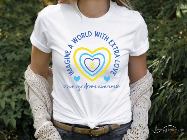Model wearing a white Down Syndrome Awareness shirt with blue and white outlined hearts and arrows in the middle. Text around the heart says "Imagine a World with Extra Love" and says down syndrome awareness in cursive at the bottom